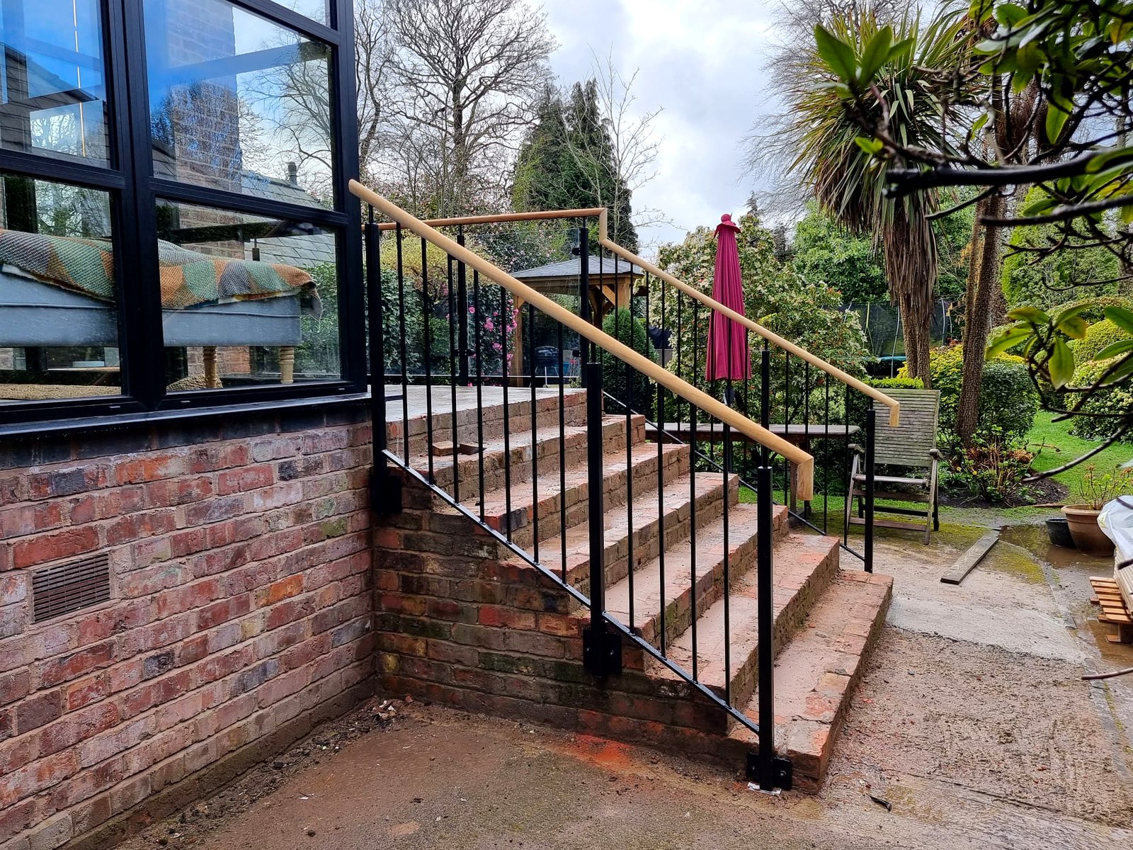 Black metal bar-infill railings with an iroko timber handrail to garden steps, Timperley, Manchester